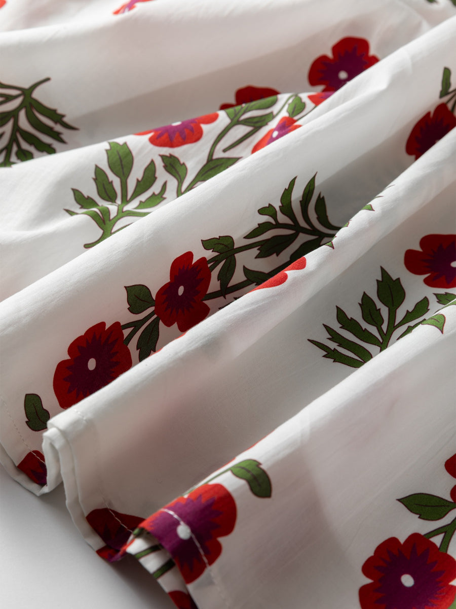 V-neck mini dress in white cotton with a red floral print and green leaves.