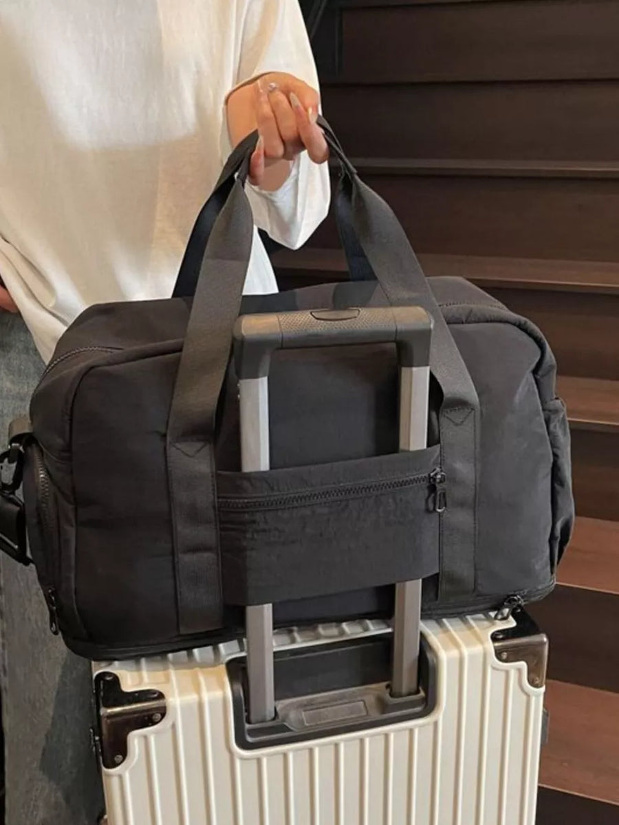 Black travel duffel bag with trolley sleeve and zippered pocket, shown on a white suitcase.