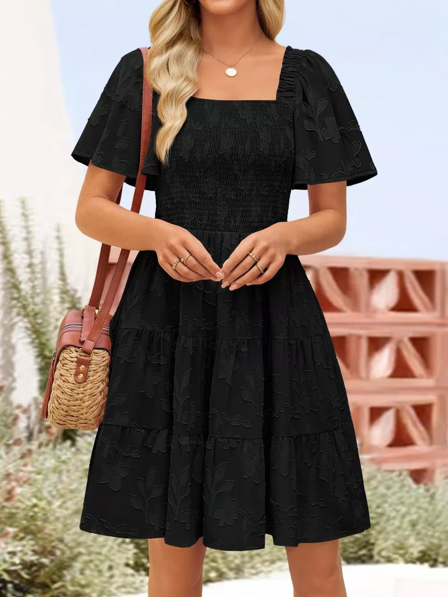 Black smocked mini dress with tiered skirt, square neckline, and flutter sleeves.