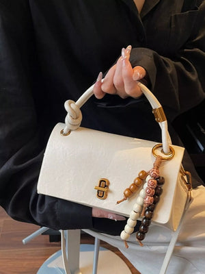 Ivory leather crossbody bag with knotted handle and beaded charm detail.