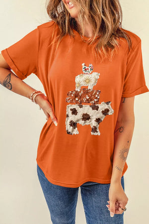 Orange short sleeve t-shirt with stacked cow, floral, and sun applique graphic.