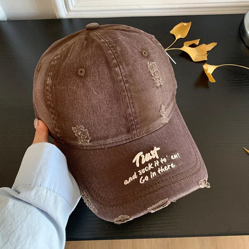 Brown distressed baseball cap with white embroidered text and frayed details