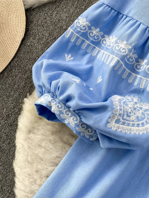 Blue blouse with white embroidery on balloon sleeves and tie neck detail.