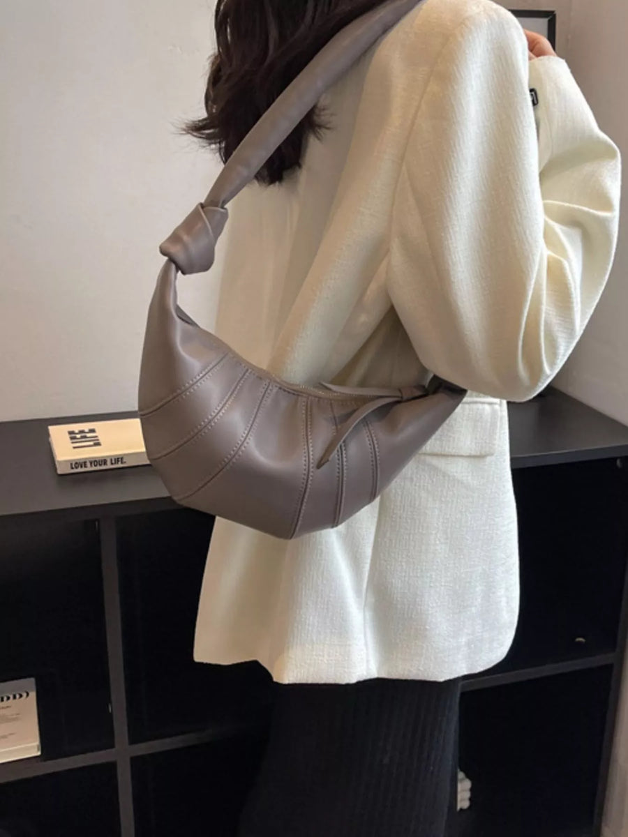 Grey hobo bag with stitched details and knotted strap, worn crossbody.
