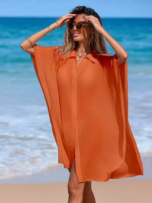 Orange button-up cover-up with short sleeves and a collared neckline, styled on a beach.