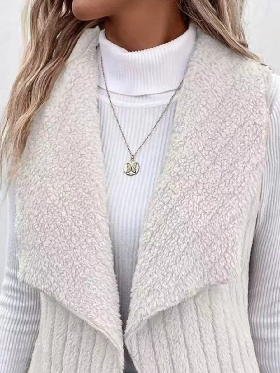 White cozy open front fleece vest with waterfall collar, worn over a turtleneck.
