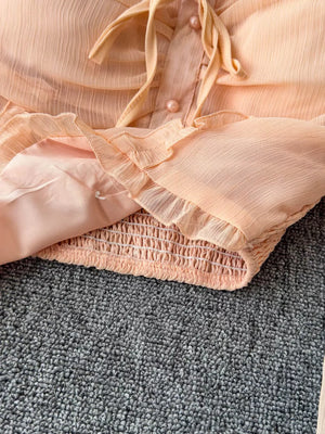 Peach maternity blouse with ruffled sleeves, tie neck, and smocked hem.