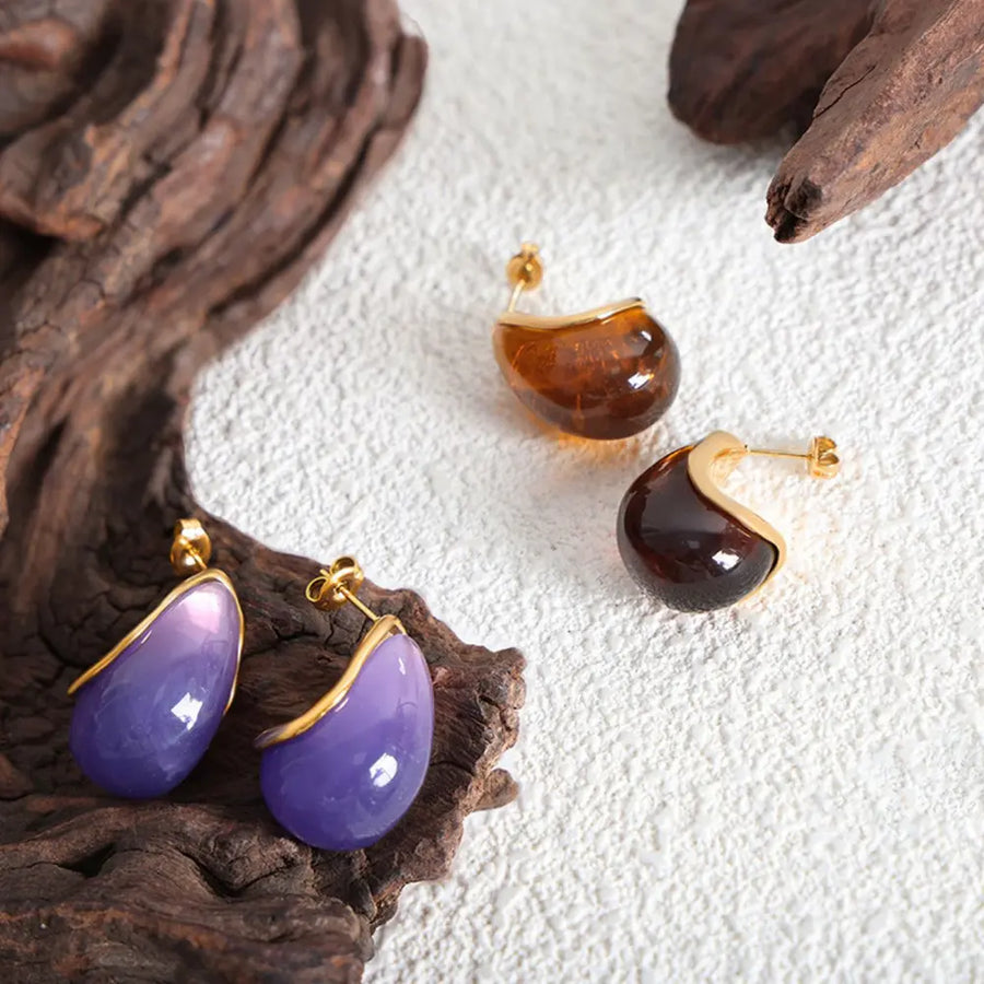 Teardrop resin stud earrings with gold trim in purple and amber tones.