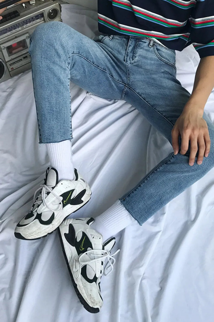 Medium wash denim jeans with raw hem, slim fit, styled with white socks and sneakers.