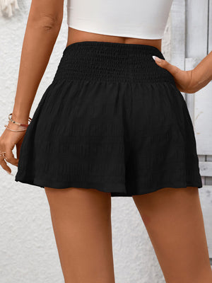 Black smocked waist drawstring shorts with textured fabric and a flared hem.