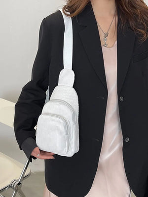 White corduroy sling bag with zip pockets, worn crossbody.