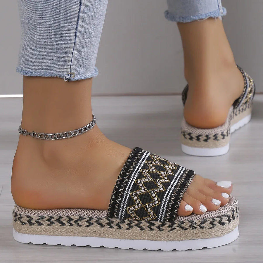 Black embroidered platform espadrille slides with woven jute sole and white pedicure.