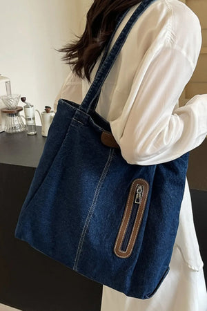 Denim shopper tote bag with leather trim and zipper pocket detail.