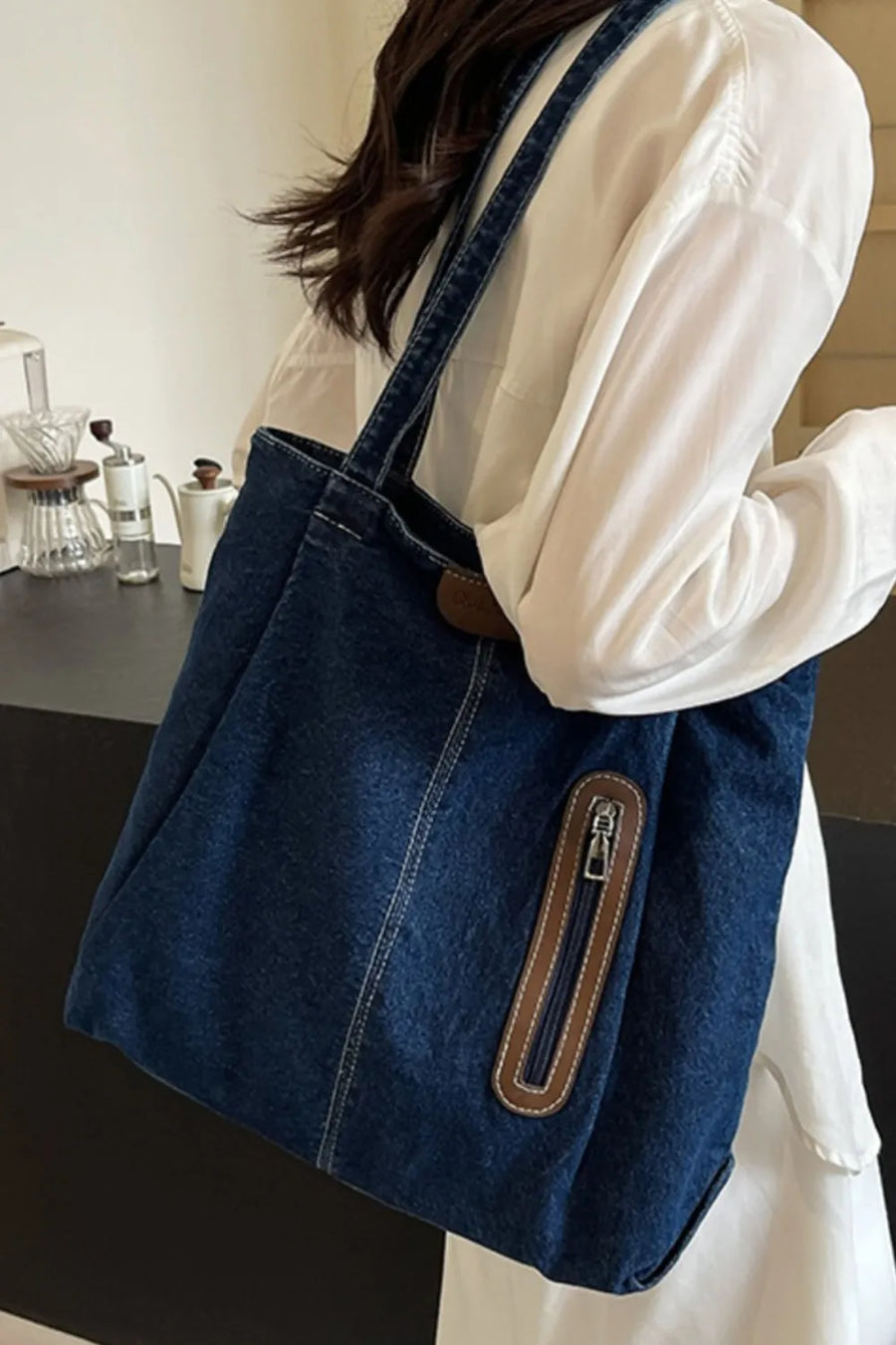 Denim shopper tote bag with leather trim and zipper pocket detail.