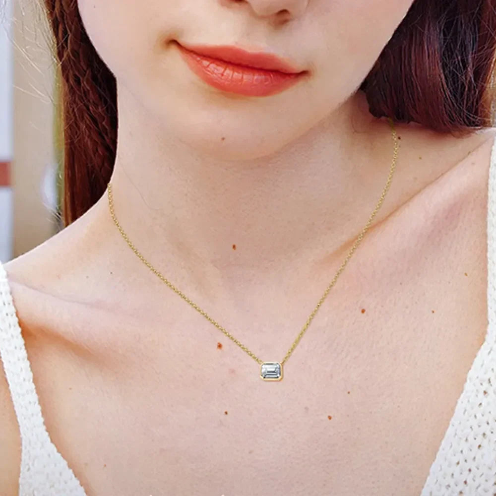 Gold bezel necklace with emerald cut moissanite pendant on a delicate chain