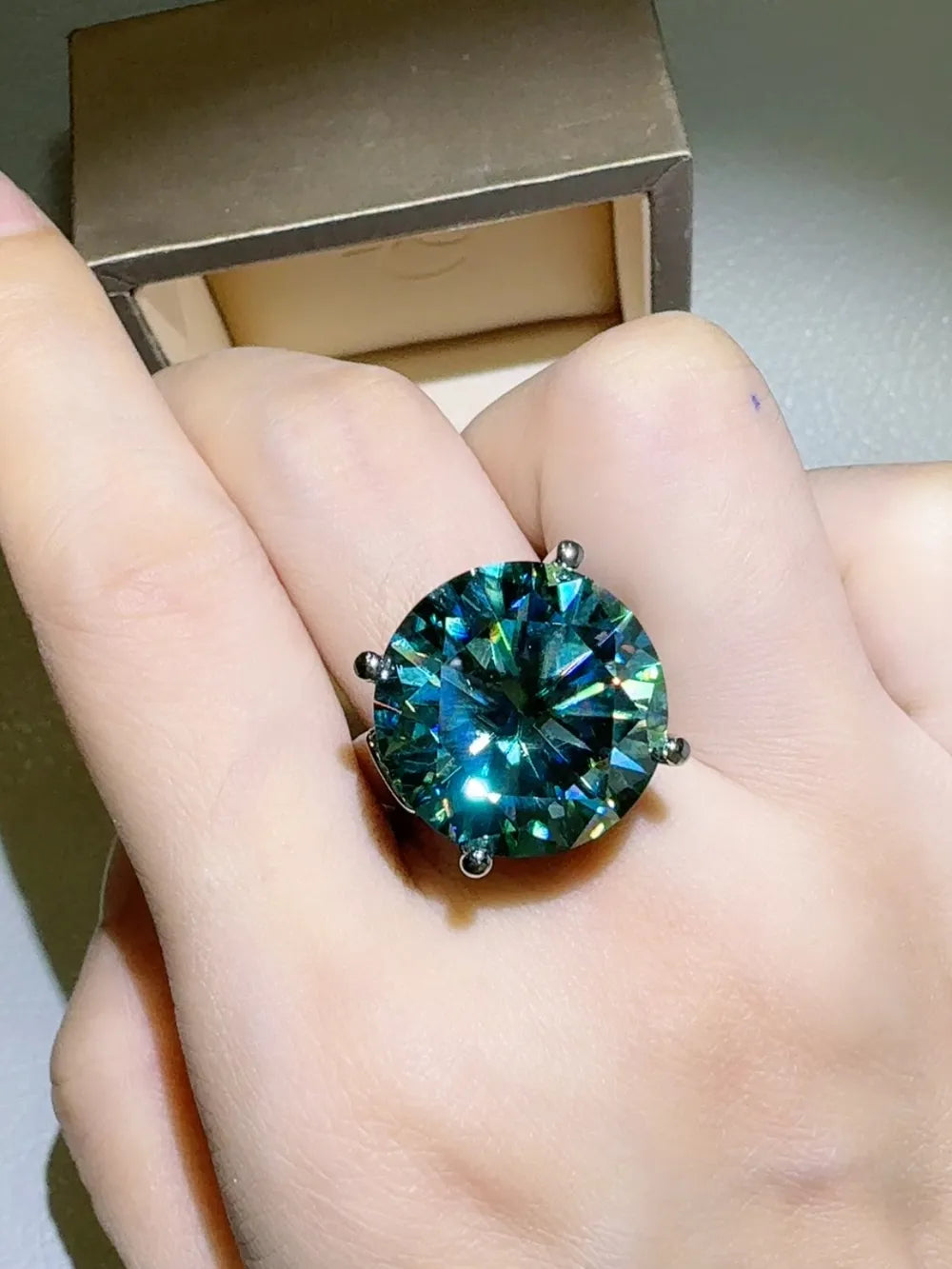 Prismatic teal statement ring with a large, round, faceted gemstone on a silver band.