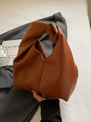 Brown leather shoulder bag with knot handle and a slouchy silhouette.