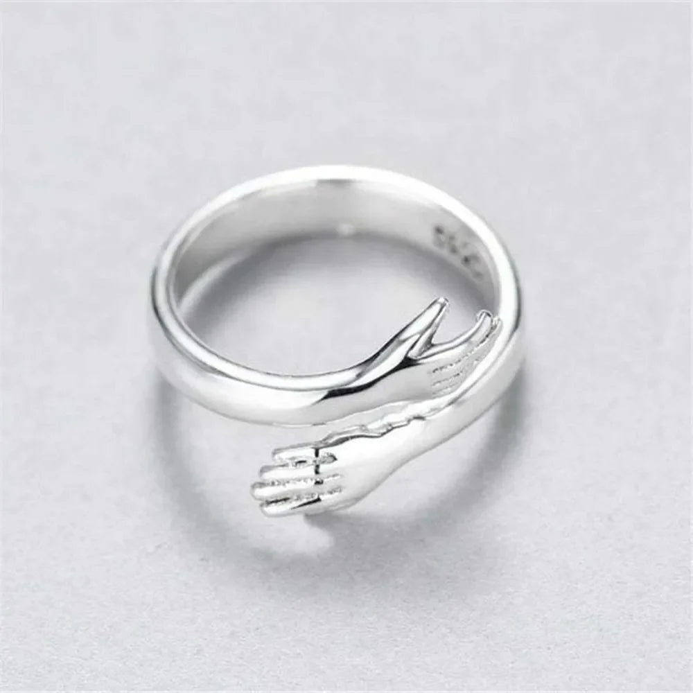 Sterling silver ring with hugging hands design, adjustable, symbolizing affection.