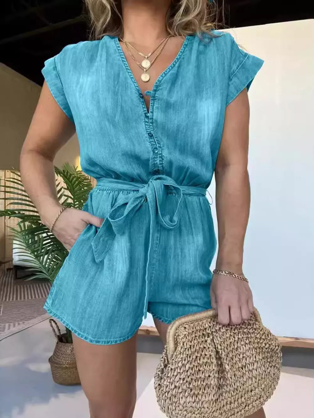 Blue tie-waist romper with V-neck, button-down front, and short sleeves.