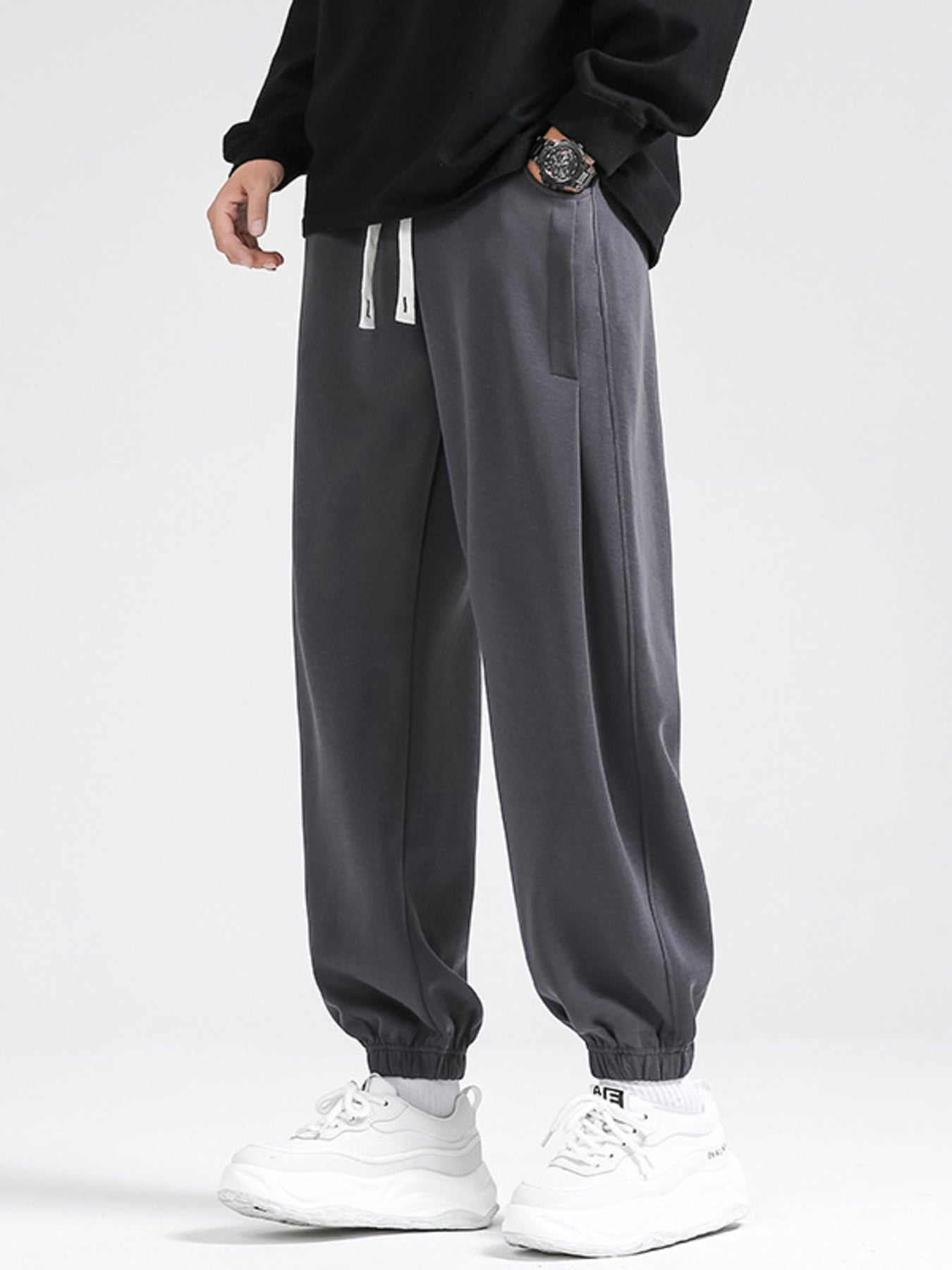 Dark gray relaxed fit sweatpants with white drawstring and cuffed ankles.