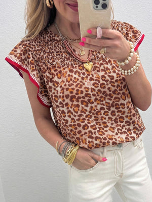 Smocked ruffled print blouse with animal print and red trim detail.