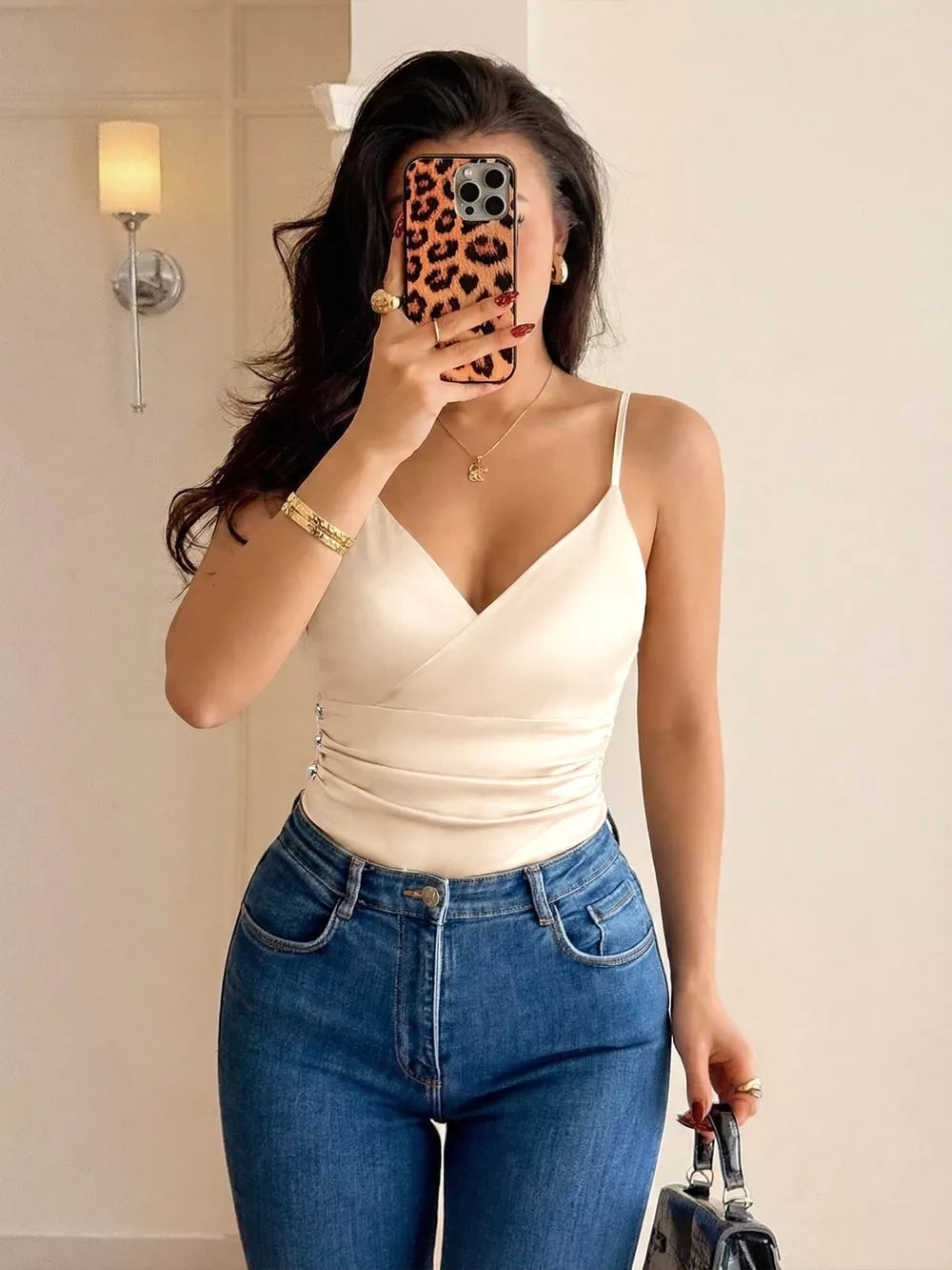 Elegant V-neck ruched bodysuit in cream with spaghetti straps and a satin finish, styled with blue jeans.
