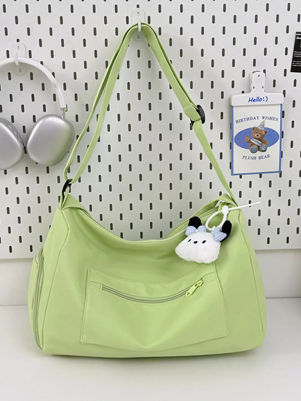 Light green travel pouch with adjustable strap and zippered pockets, featuring a cute plush charm.