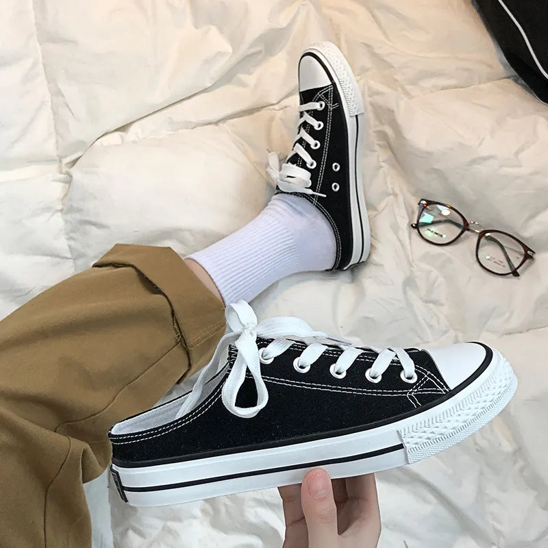 Black canvas mule sneakers with white contrast trim and laces.