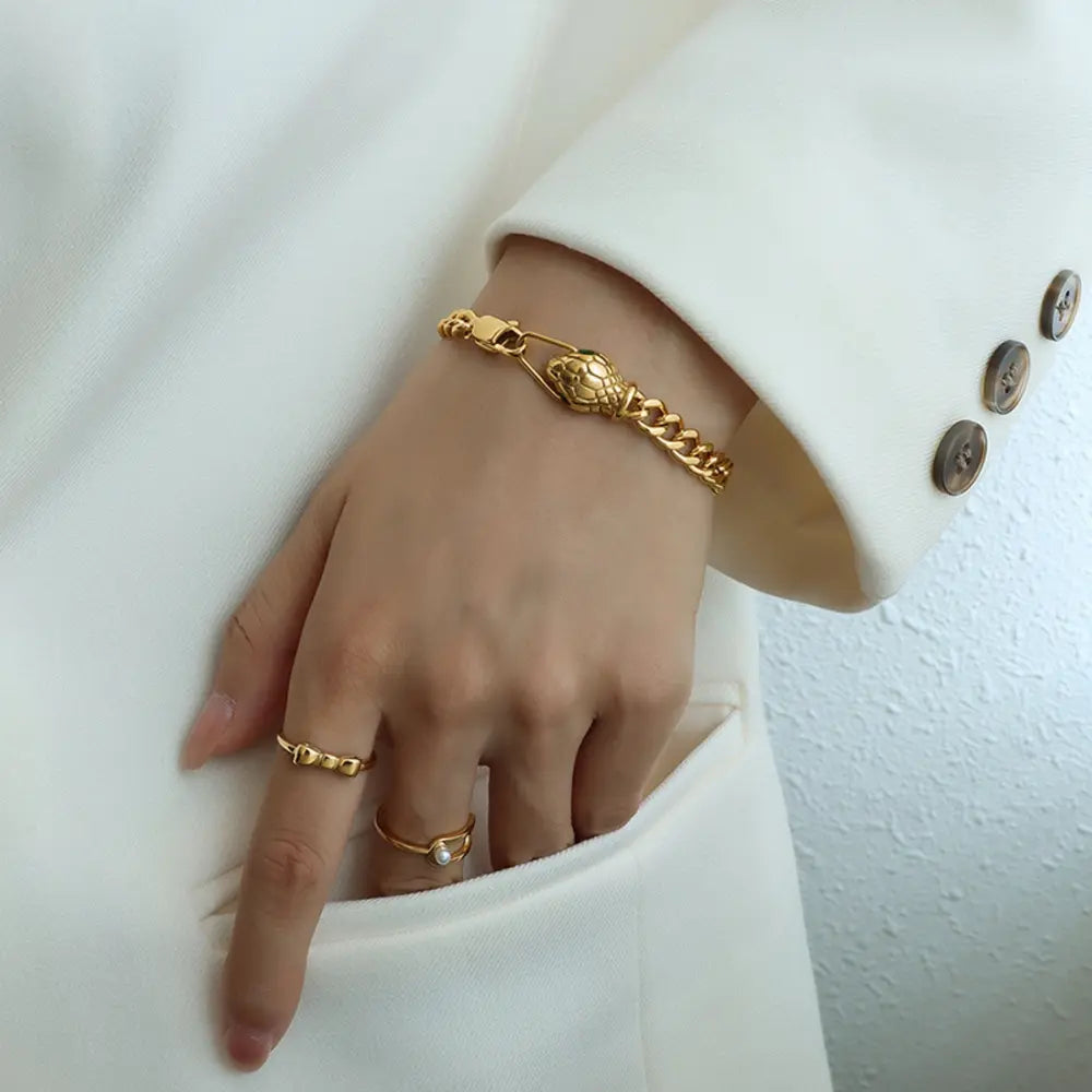 Gold serpentine chain bracelet with snake head clasp, worn with rings.