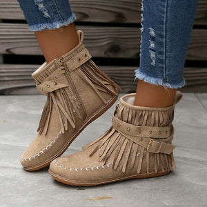 Beige suede ankle boots with fringe, studs, and buckle detail.
