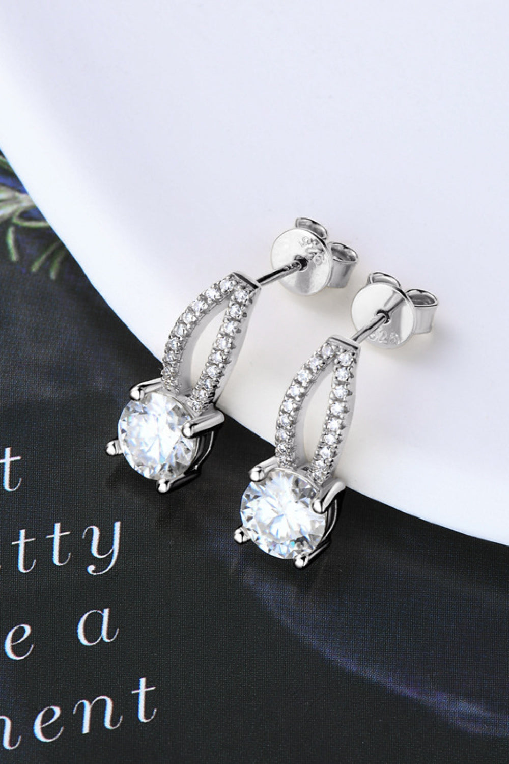 Silver stud earrings with a dangling design featuring a large round moissanite stone and a pave-set crystal accent.