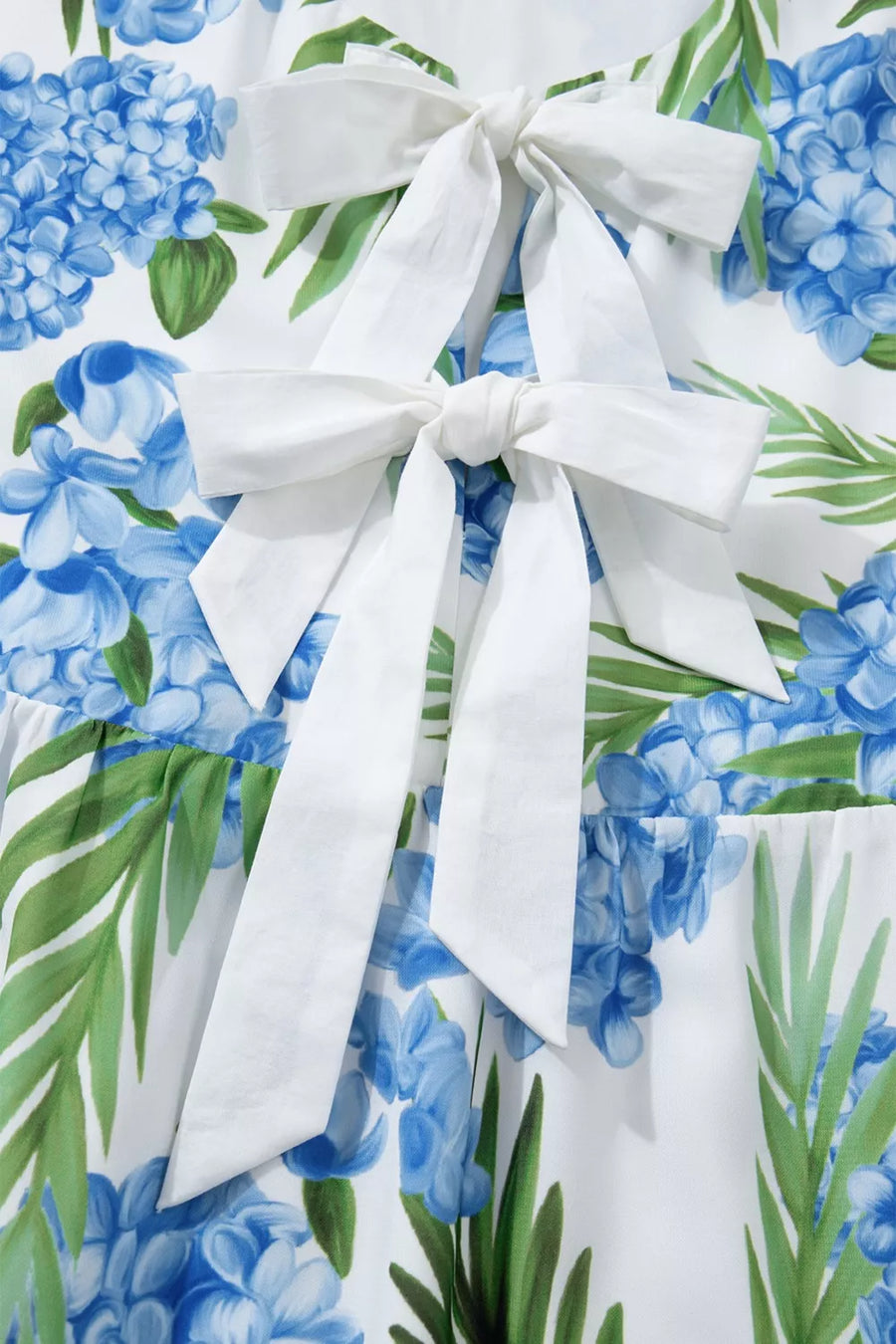 Ruffled mini dress with hydrangea and palm print, featuring white bow details.