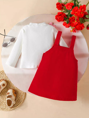Red corduroy pinafore dress with white ribbed long sleeve top.