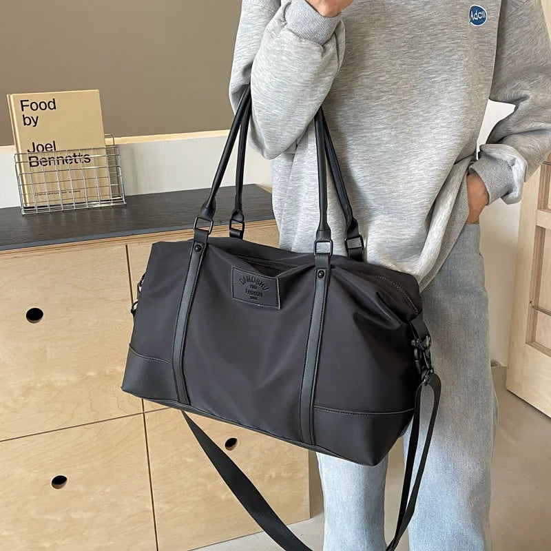Black duffel bag with leather trim and shoulder strap, perfect for gym or travel.