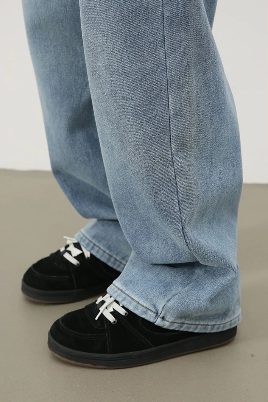 Oversized fade wash denim jeans in medium blue, shown with black sneakers.