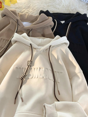 Cream drawstring hoodie with embossed text and contrast drawstrings.