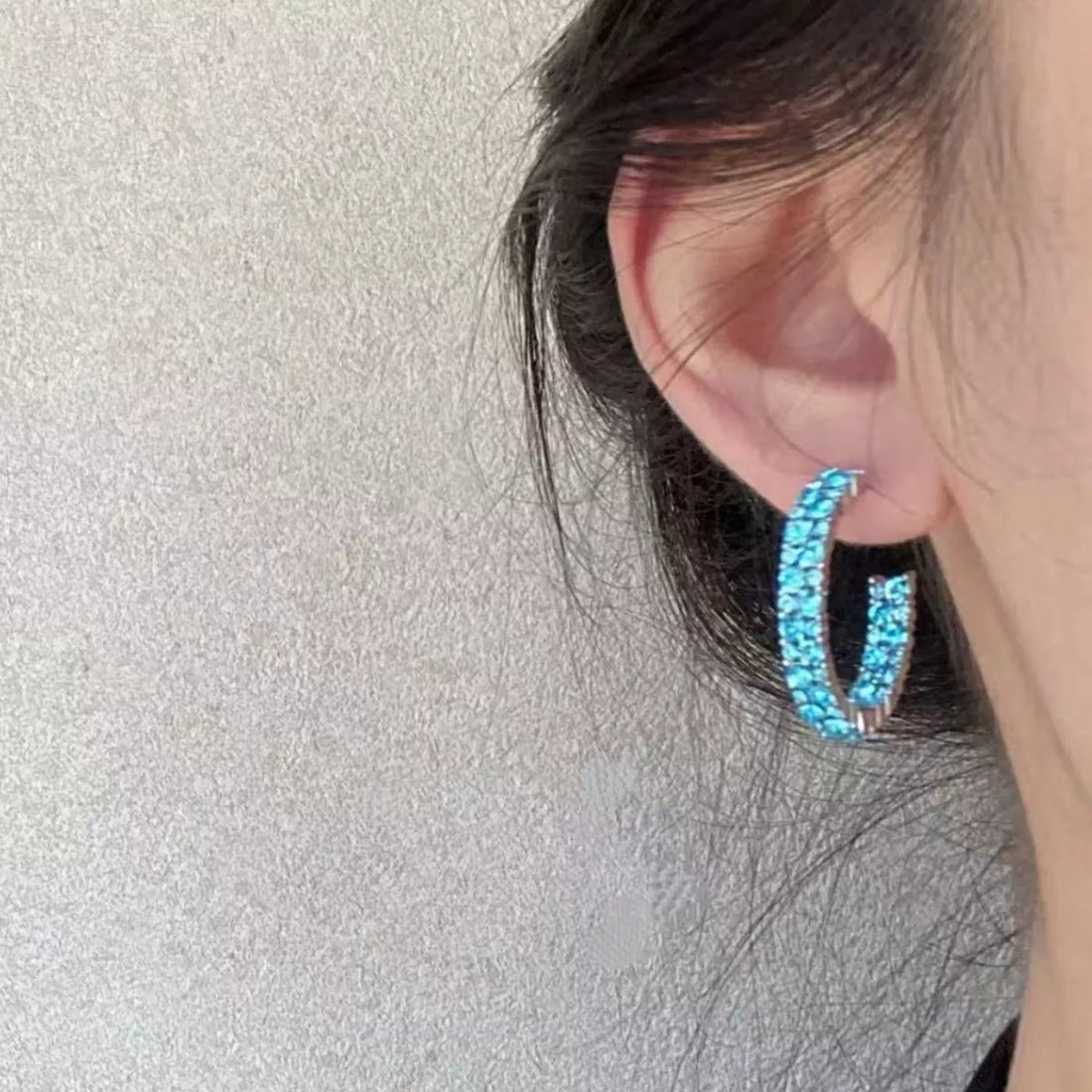 Sparkling pastel blue hoop earrings with crystal accents on an adult woman's ear.