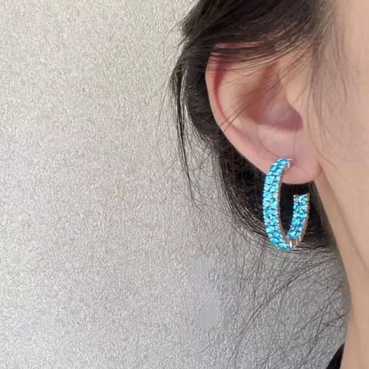 Sparkling pastel blue hoop earrings with crystal accents on an adult woman's ear.