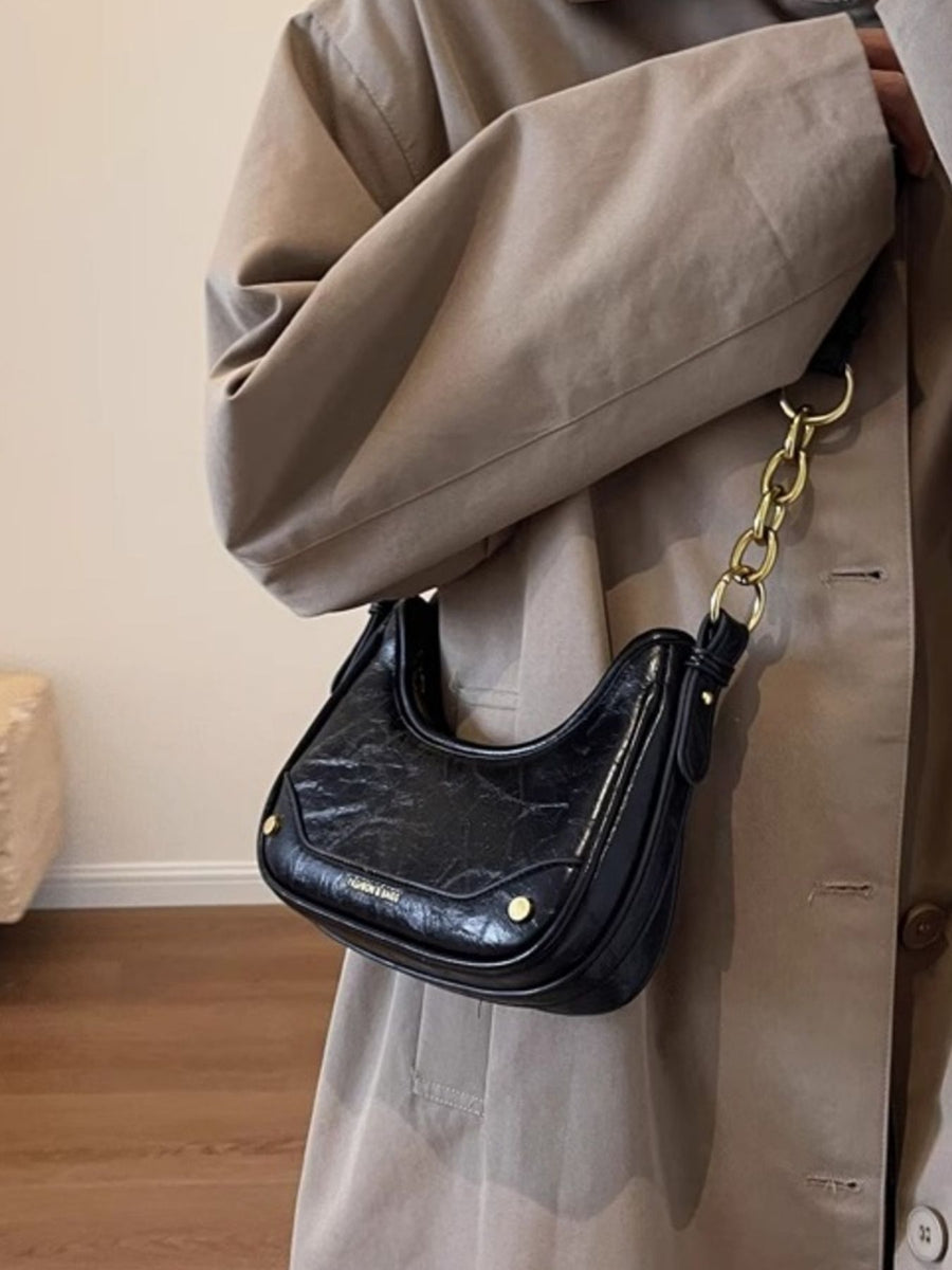 Black shoulder bag with chunky gold chain accent and crescent shape.