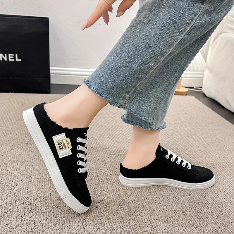 Black denim mule sneakers with raw edges and white laces.