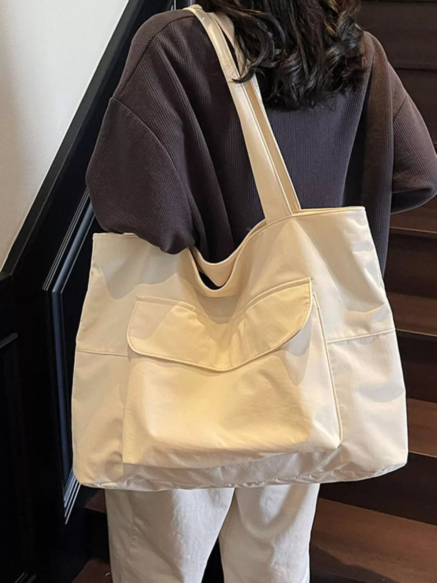 Spacious cream nylon shoulder bag with flap and front pockets.