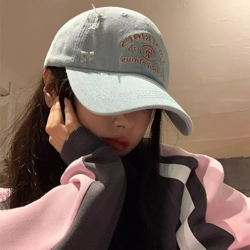 Light blue denim baseball cap with distressed details and red embroidered text.