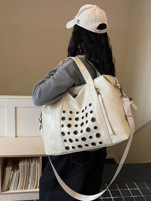 Cream leather travel bag with eyelet details and a detachable strap.