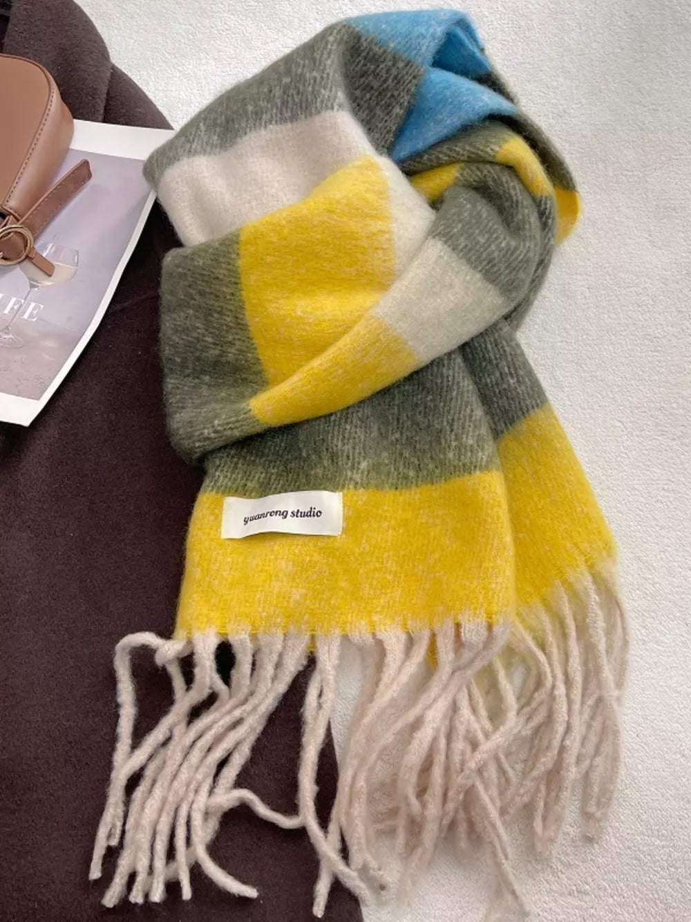 Plush multi-patterned scarf in yellow, green, blue, and white with fringe details.