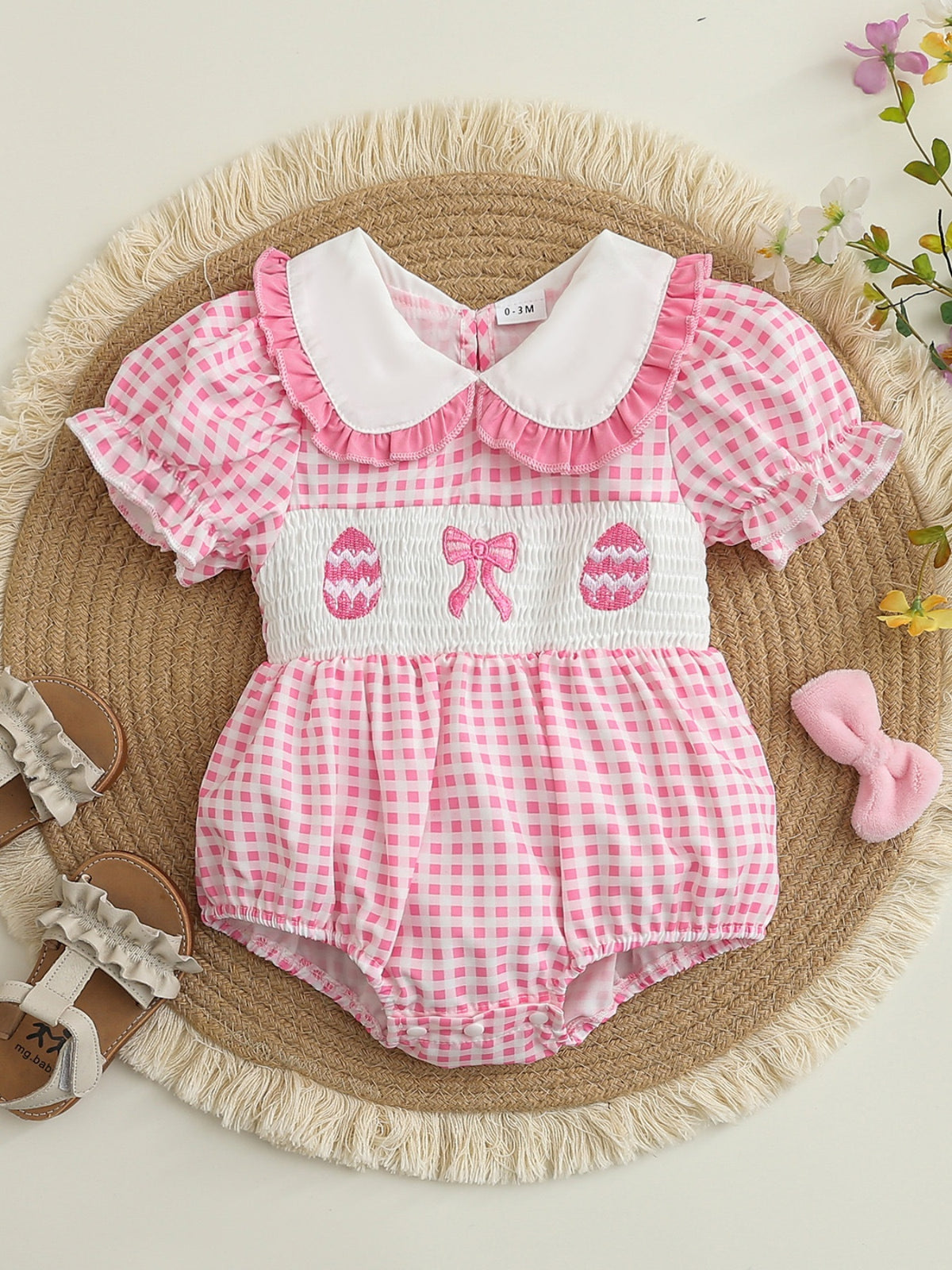 Pink gingham baby romper with smocked waist, embroidered eggs, bow, and ruffled collar.