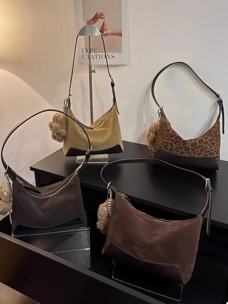 Adjustable strap shoulder bags in taupe, leopard print, and brown suede with fuzzy charms.