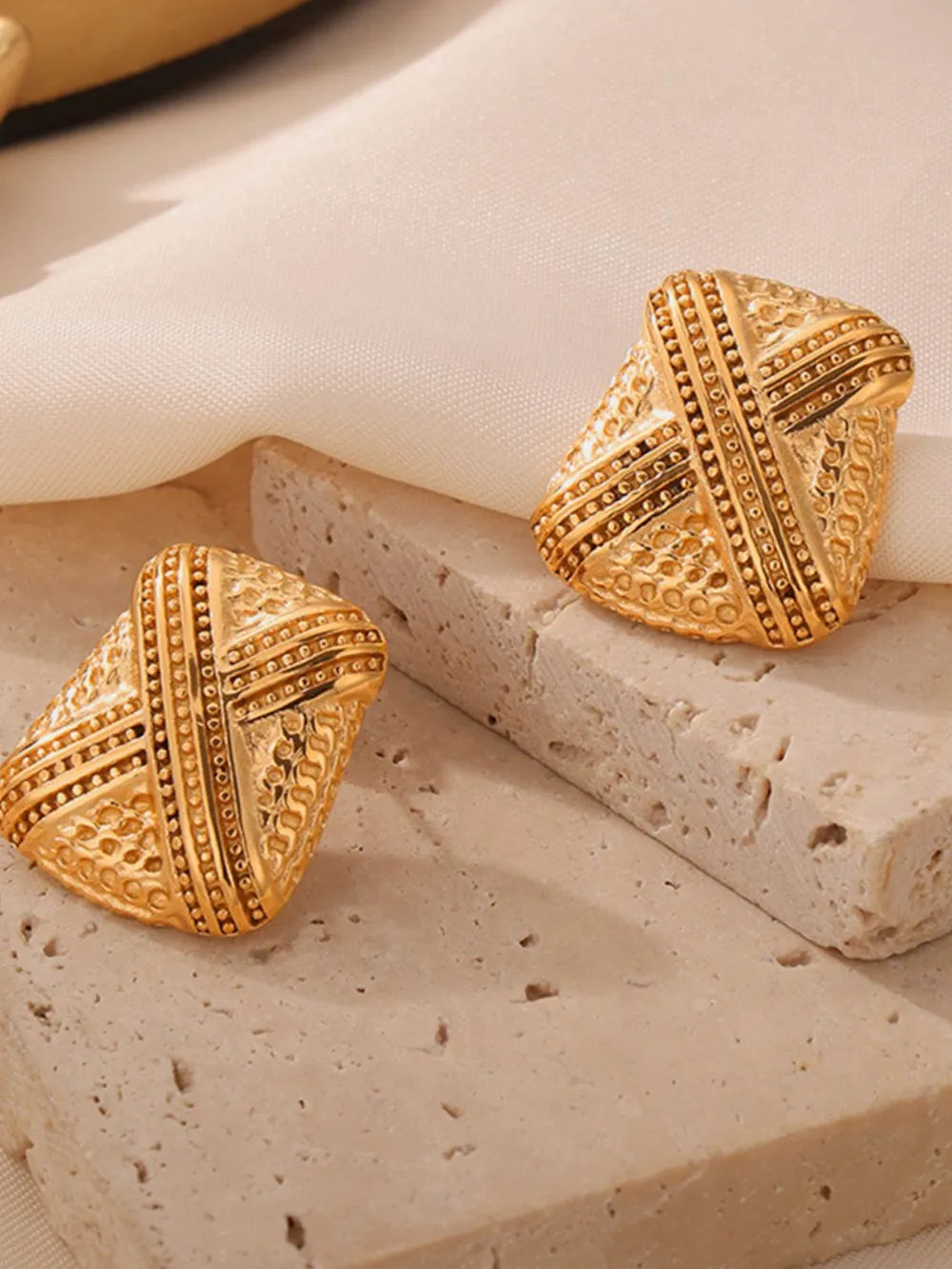 Sculptural gold-tone earrings with intricate embossed patterns and beaded trim.