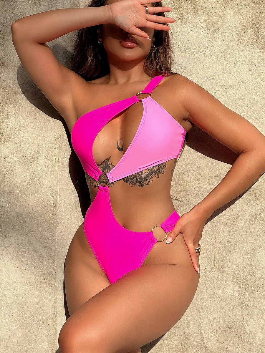 Hot pink one-piece swimsuit with asymmetric neckline, cut-out detail, and gold ring accents.