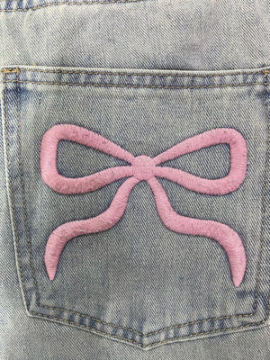 Light wash denim jeans with a pink embroidered bow detail on the back pocket.