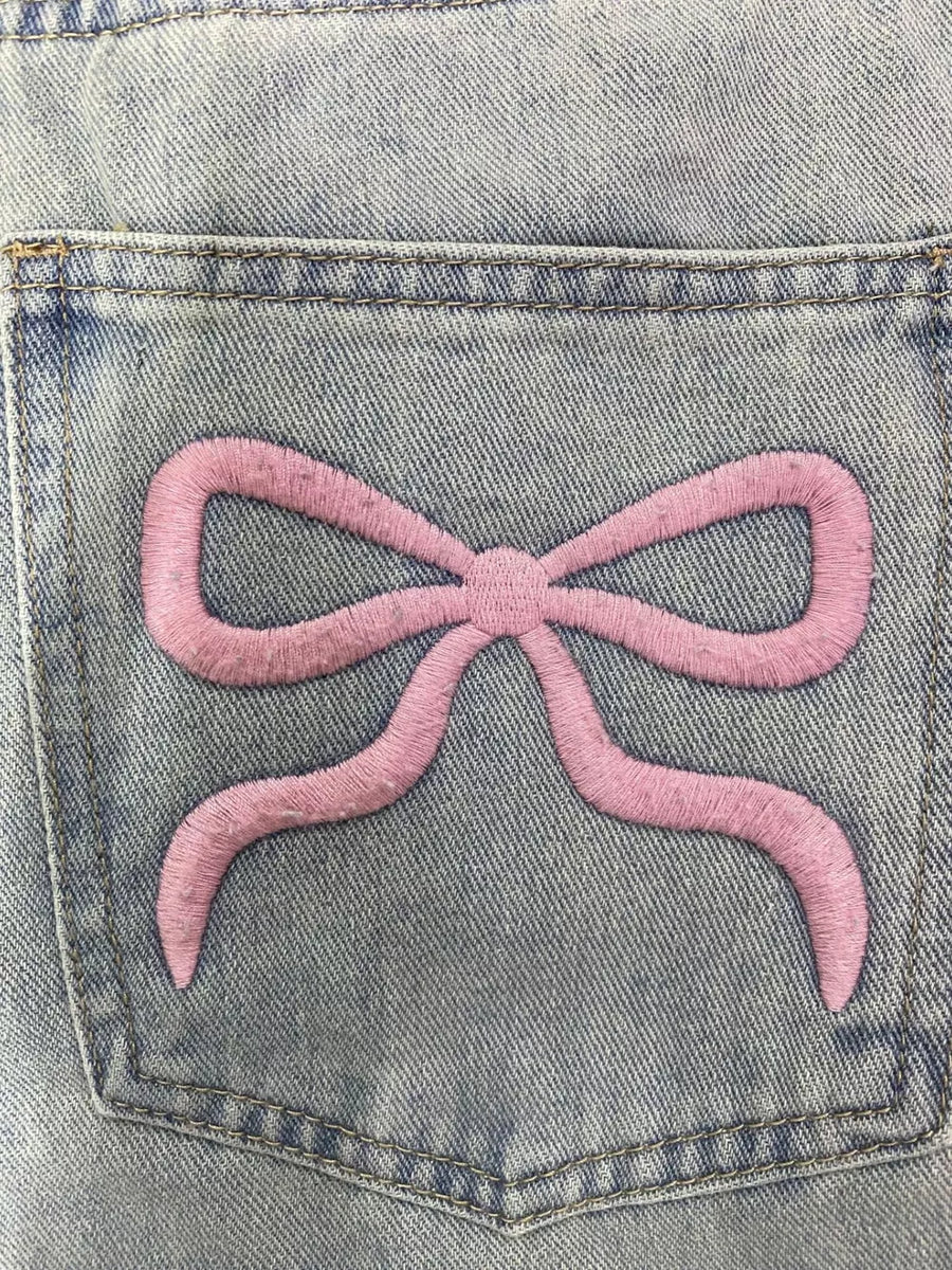 Light wash denim jeans with a pink embroidered bow detail on the back pocket.